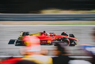 Автомобіль Формули-1 Ferrari на швидкісній трасі, зображений у русі з пейзажем у фоновому режимі, показує динаміку гонки та технічний дизайн машини.