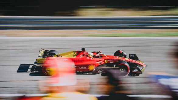 Автомобіль Формули-1 Ferrari на швидкісній трасі, зображений у русі з пейзажем у фоновому режимі, показує динаміку гонки та технічний дизайн машини.