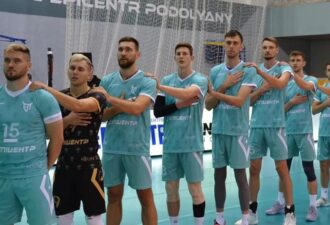 Команда волейболістів в момент виконання гімну, стоячи в ряд, одягнені в бірюзову спортивну форму з написом "Епішентр", на фоні ігрового майданчика.