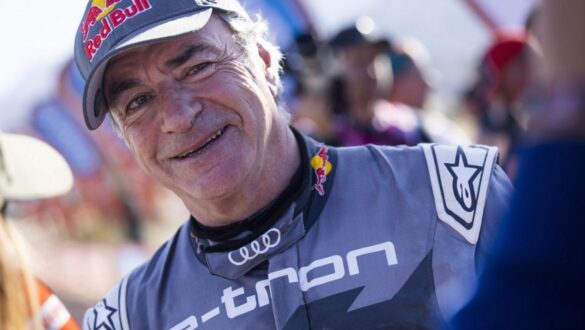 Портрет гонщика у спортивному костюмі з логотипом Audi та головним убором Red Bull. Чоловік усміхається на фоні змагань. Загальний настрій оптимістичний, відображає атмосферу спортивного заходу.